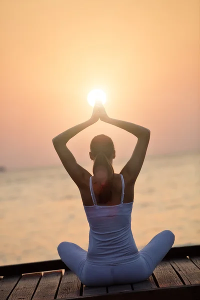 Gün batımında plajda yoga yapan genç bir kadın. — Stok fotoğraf