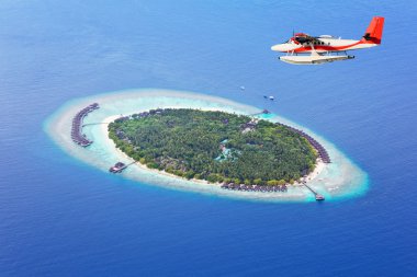 Sea plane flying above Maldives islands clipart