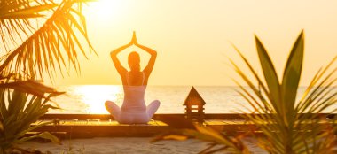 Young woman practicing yoga on the beach at sunset clipart