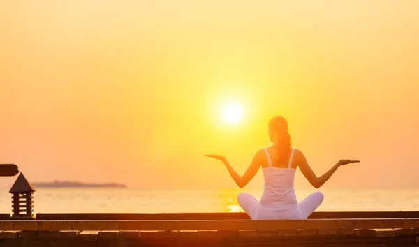 Gün batımında plajda yoga yapan genç bir kadın. — Stok fotoğraf