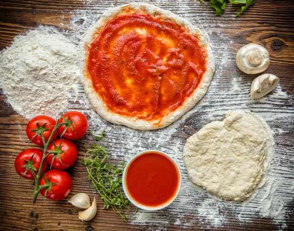 Pizzateig mit Tomatensauce auf Holztisch — Stockfoto