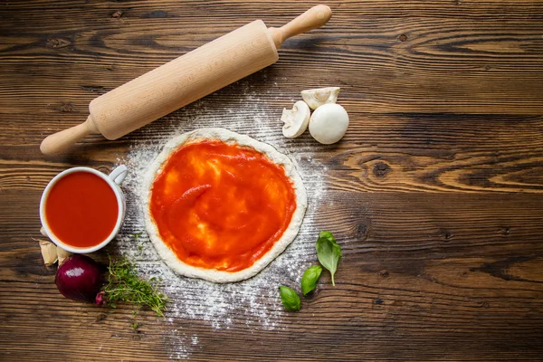 Massa de pizza com molho de tomate na mesa de madeira — Fotografia de Stock