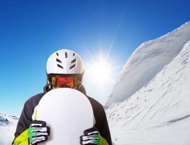 Snowboarder holding his snowboard off piste clipart