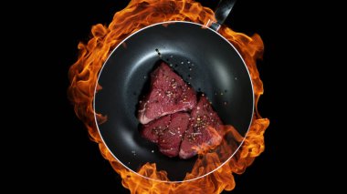 Biftek tavada, alevler arka planda. Yüksek açılı et hazırlama, stüdyo çekimi.