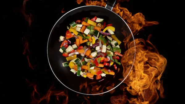 Mix vegetable in pan, flames on background. High angle view of meat preparation, studio shot.