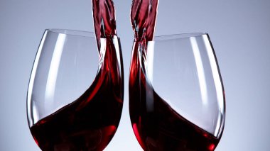 İki kadeh kırmızı şarap birbirine çarpıyor, gri arka planda izole edilmiş.