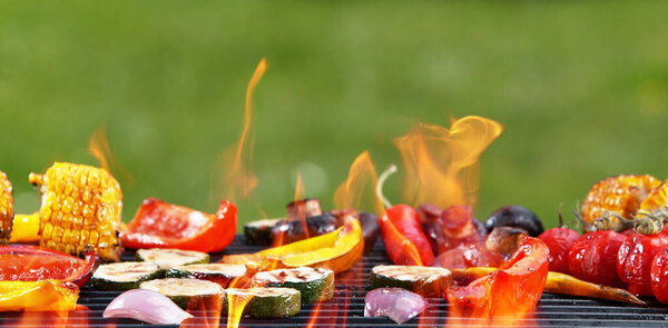 Assorted delicious grilled vegetables placed on grill with fire. Outdoor garden barbecue background.