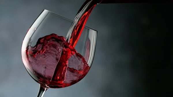 Glass of red wine on dark background closeup. Studio clear shot of pouring wine into goblet.