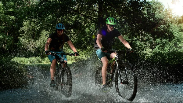 Mountain Bikers Acelerando Através Córrego Floresta Respingo Água Movimento Congelamento — Fotografia de Stock