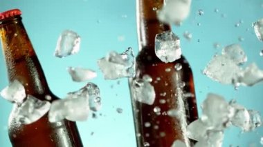 Mavi arka planda buzla birlikte düşen bira şişelerinin süper yavaş çekimleri. Hız rampası etkisi. Yüksek hızlı sinema kamerası, 1000 fps..