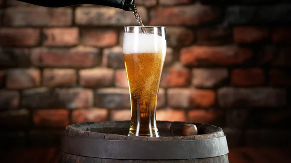 Pouring beer into pint, stylish brick wall on background. Fresh beverages and pub backgorund.