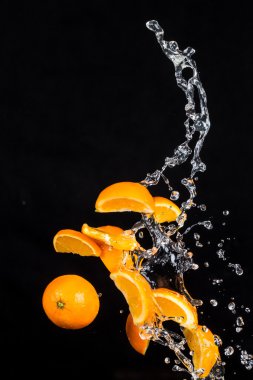 Oranges with water splashes on black background clipart