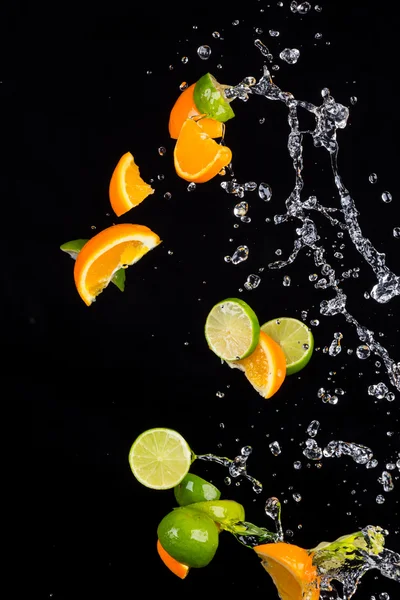 Limoenen en sinaasappels met water spatten op zwart — Stockfoto