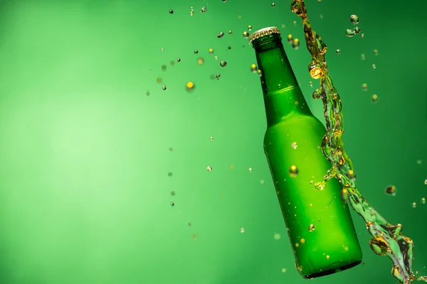 Bottle of beer with splash, on green background — Stock Photo, Image