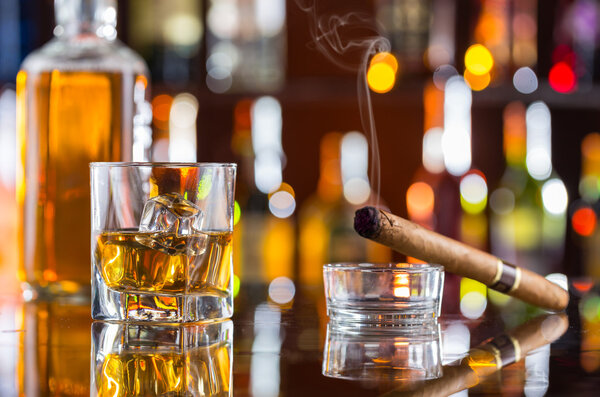 Whiskey drink with smoking cigar on bar