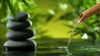 Stack of black spa stones beside bamboo water fountain creating ripples on a calm surface. Tranquil scene for wellness, relaxation, and meditation.