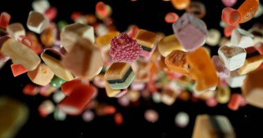 Siyah arka planda havada uçuşan renkli şekerler. Canlı renklerle dinamik makro çekim, sığ alan derinliği ve hareketsiz durma. Yemek, reklam ve yaratıcı tasarım için mükemmel..
