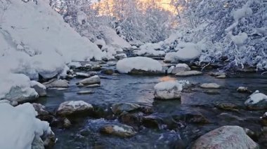 Karla kaplı bir alp deresinin üzerinde huzurlu bir ağır çekim uçuşu. Akan buzlu su, donmuş kayalar ve taze kar dinlenme, meditasyon ve doğa görselleri için ideal bir kış atmosferi yaratır..