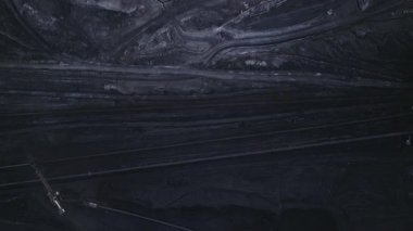 Büyük maden kazıcılarını ve kömür taşıma makinelerini geçen aktif bir açık kömür madeninin hava üstgeçidi, ölçeği, tozu ve endüstriyel gücü vurguluyor.
