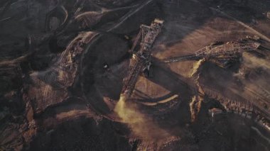 Açık bir kömür madeninde çalışan büyük bir kazıcının geniş hava görüntüsü. Dev maden makinesi aktif bir sanayi bölgesinde sürekli kömür ve toprak çıkarıyor..