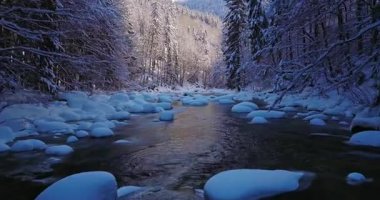 Karla kaplı bir alp deresinin üzerinde huzurlu bir uçuş. Akan buzlu su, donmuş kayalar ve taze kar dinlenme, meditasyon ve doğa görselleri için ideal bir kış atmosferi yaratır..