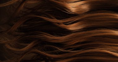 Dalgalı kahverengi saçların soyut dokusu zarif doğal dalgalar ve kıvrımlar oluşturuyor. Organik hareket, yumuşak ışık ve zengin tonlar sinematik güzellik arkaplanı ya da lüks görsel element oluşturur.