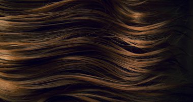 Dalgalı kahverengi saçların soyut dokusu zarif doğal dalgalar ve kıvrımlar oluşturuyor. Organik hareket, yumuşak ışık ve zengin tonlar sinematik güzellik arkaplanı ya da lüks görsel element oluşturur.