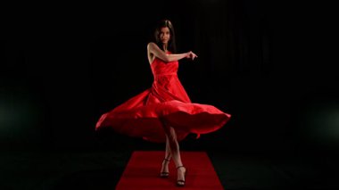 Yakut kırmızısı elbiseli, çarpıcı siyah saçlı kadın ve yüksek topuklu ayakkabı giyen zarif siyah arka plan pozu, dramatik ve zarif bir moda efekti için süper yavaş çekimde yakalandı..