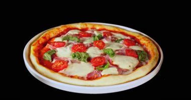 Pişirme işlemi sırasında pizza dönüşümlü, siyah arka planda izole edilmiş. Sinema stüdyosunun çekimleri yemek pişirme süresinin ilerlemesini, erimiş peyniri ve taze malzemeleri gösteriyor. Yemek, yemek ve restoran kavramları için mükemmel..