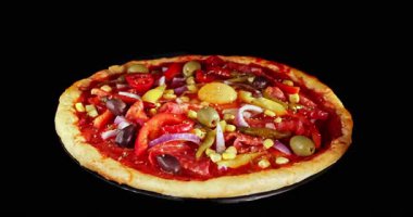 Pişirme işlemi sırasında pizza dönüşümlü, siyah arka planda izole edilmiş. Sinema stüdyosunun çekimleri yemek pişirme süresinin ilerlemesini, erimiş peyniri ve taze malzemeleri gösteriyor. Yemek, yemek ve restoran kavramları için mükemmel..