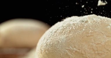 Mayalanmış hamurun sinematik hareketli çekimi siyah zemin üzerinde izole edilmiş ve un süper yavaş çekimde düşüyor, 1000 fps. Dinamik pişirme konsepti, zanaatkar ekmek hazırlama ve doku detayı.