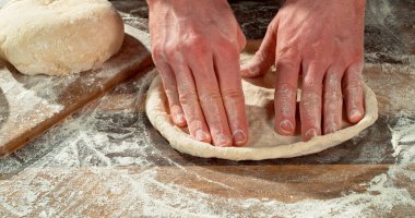 Taze pizza hamurunu un ahşap bir masada şekillendiren ellerin yakın çekimi. Ayrıntılı doku, kırsal atmosfer ve otantik hazırlık süreci. Ev yapımı pizza ve zanaatkar pişirme kavramı.