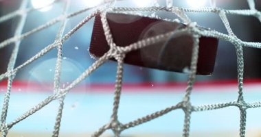 Buz hokeyi diski, çarpışma anında patlayan buz parçacıkları ve arka planda bulanık bir kış stadyumu ve buz pateni pisti ile 1000 fps hızla gol ağına çarpıyor. Hız rampası.