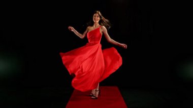 Yakut kırmızısı elbiseli çarpıcı siyah saçlı kadın ve yüksek topuklu zarif siyah arka plan pozu, Süper Yavaş Çekimde Yakalandı. Hız Rampası Efekti.