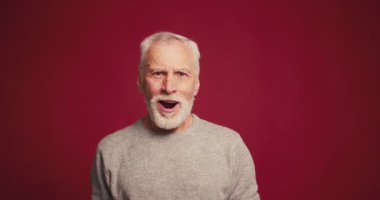 Zarif, ağzı açık, kırmızı arka planda izole kameraya bakan olgun sakallı adamı heyecanlandırır. Günlük giysiler içinde aşırı neşeli bir erkek. Alışveriş, satış, reklam konsepti