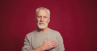 Mutlu, gülümseyen, mutlu yaşlı sakallı adamın portresi kırmızı arka planda izole edilmiş kameraya el ele bakıyor. Minnettarlık kavramı