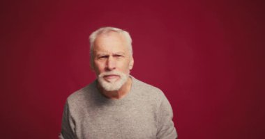 Kırmızı arka planda izole edilmiş kameraya bakan mutlu, yakışıklı, yaşlı, sakallı adam. Reklam kavramı