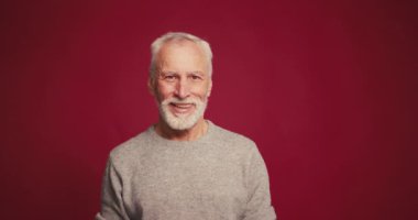 Gülümseyen, mutlu kıdemli bir adamın portresi. Kırmızı arka planda izole edilmiş fotokopi alanına bakıyor. Alışveriş, reklam konsepti.