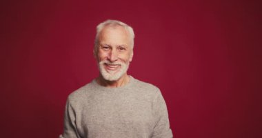 Kendine güvenen yaşlı sakallı bir adamın portresi kırmızı arka planda izole edilmiş bir şekilde kameraya bakıyor. İşaret dili kavramı