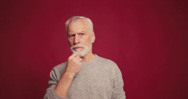 Dikkatli, ciddi, olgun sakallı bir adam kırmızı arka planda izole edilmiş kafaya dokunmayı düşünüyor. Reklam kavramı