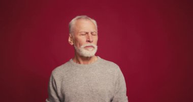 Mutsuz, ciddi, kıdemli bir adam kırmızı arka planda izole edilmemiş, başını sallayan kameraya bakıyor. Olumsuz duygular konsepti