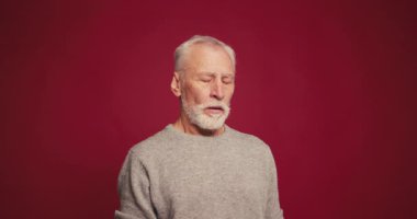Kırmızı arka planda izole edilmiş kameraya bakarak esneyen yaşlı bir adamın portresi. Yorgun yaşlı erkek uyumak istiyor. Rahatlatıcı kavram