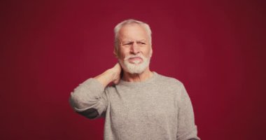 Üzgün, gri saçlı, boynu ağrıyan, kırmızı arka planda tek başına duran son sınıf öğrencisi. Olgun erkek çıkıntısı var. Sağlık hizmeti kavramı