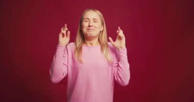 Mutlu, gülümseyen orta yaşlı, parmakları çapraz olan bir kadın kırmızı arka planda gözleri kapalı bir dilek diliyor. Noel konsepti