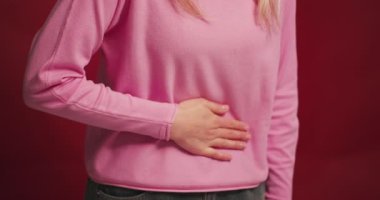 Üzgün, sarışın, orta yaşlı, karnı ağrıyan bir kadın, kırmızı arka planda kendini kötü hisseden bir spazm. Sağlık hizmeti kavramı