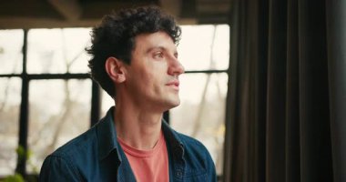 Yakışıklı bir adam pencereden dışarı bakıyor ve sonra kafasını kameraya doğru çeviriyor, modern iş birliğinden memnuniyet ve güven yayıyor. Reklam kavramı