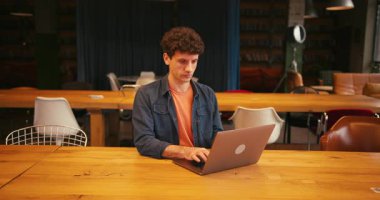 Üniversite kütüphanesinde ya da modern çalışma alanında dizüstü bilgisayarla çalışan erkek öğrencilere odaklanmış. Kopya yazarı klavyeye yazı yazıyor. Çevrimiçi teknoloji kavramı