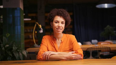 Modern ofiste oturmuş kameraya bakarak şık giyinen, kendinden emin, gülümseyen, Afro-Amerikan iş kadınının portresi. İş konsepti