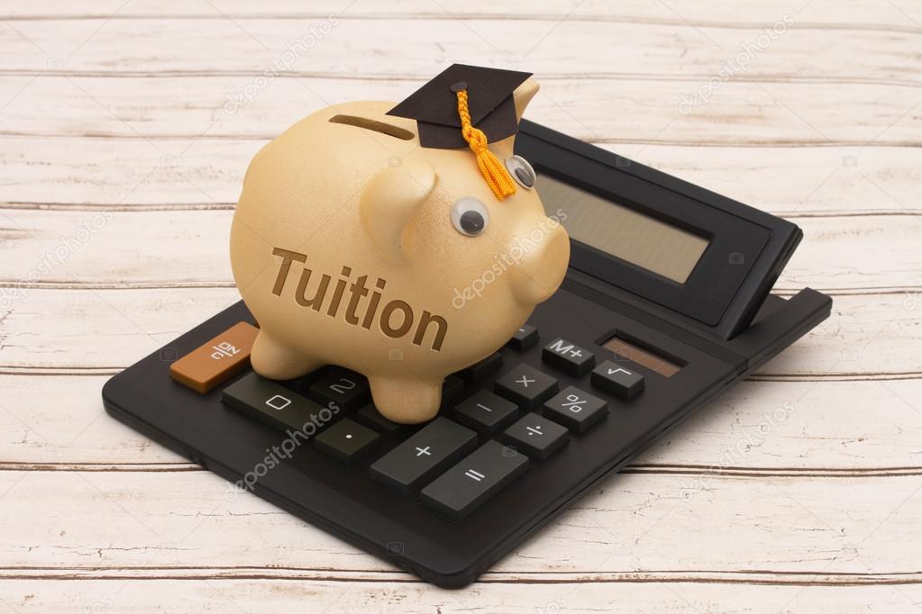 A golden piggy bank with grad cap and calculator on wood backgro