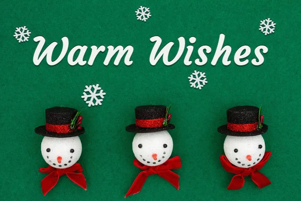 Warm wishes greeting with Christmas snowmen with top hats on green felt